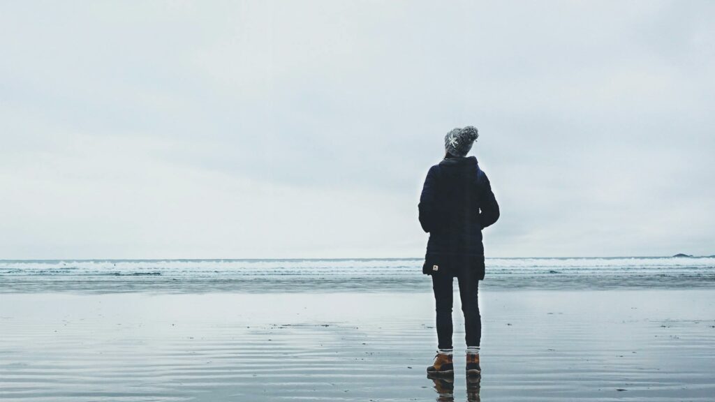 Frau am Strand schaut verträumt in den Himmel